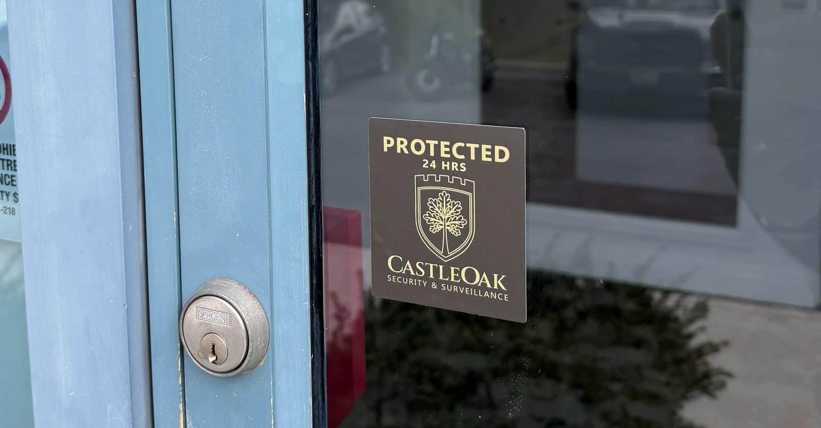 CastleOak Protected 24 Hrs decal and commercial door lock at a business entrance